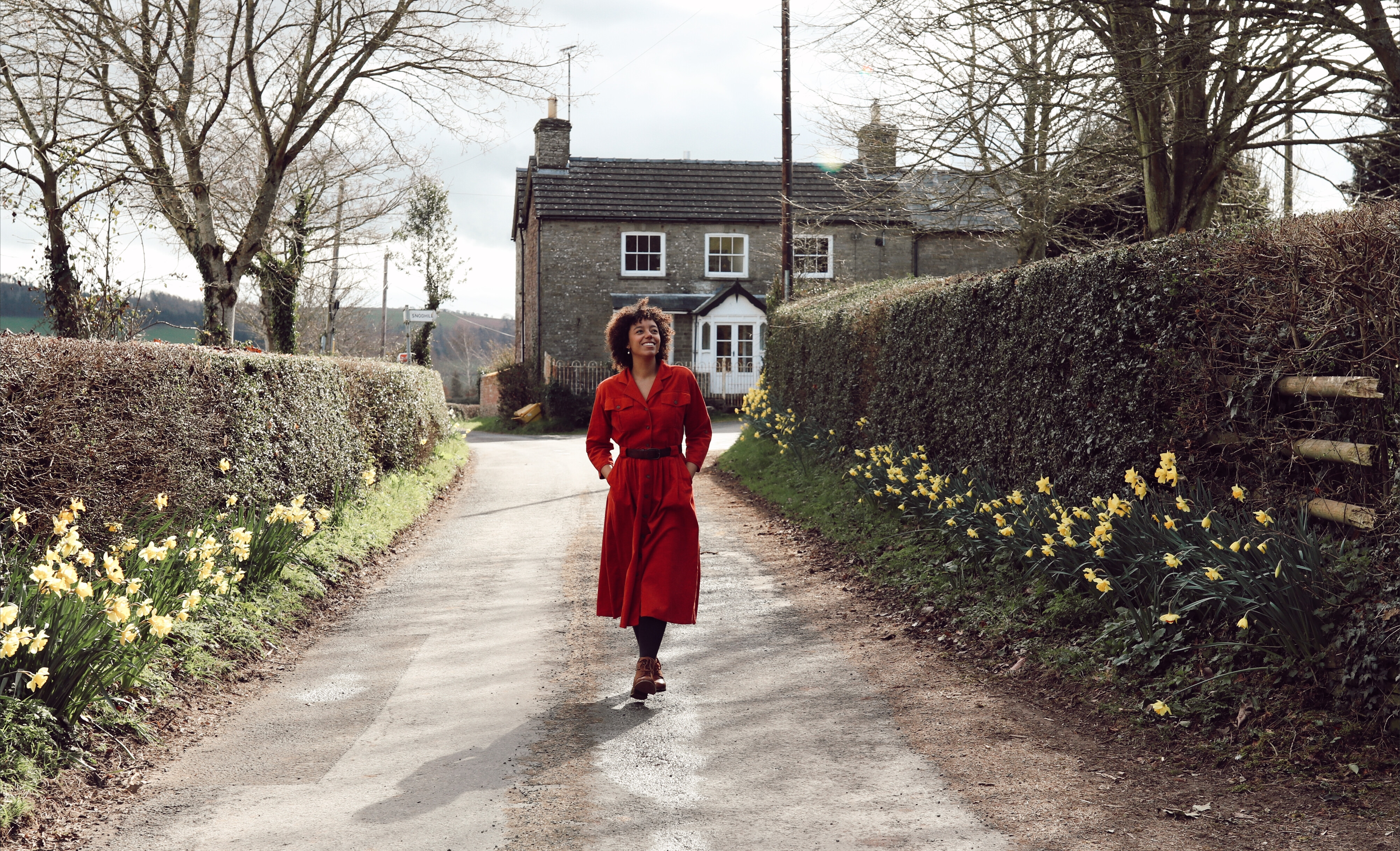 A woman in a red dress walks down the lane in Kilpeck