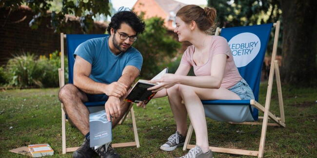 A male and female sitting on Ledbury Poetry branded deckchairs and reading a book together