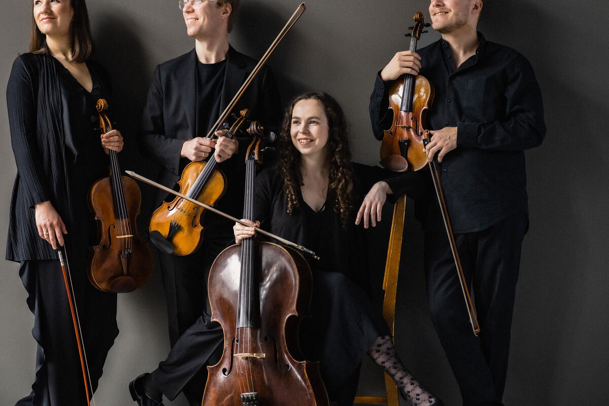 Four musicians standing against a wall with stringed instruments