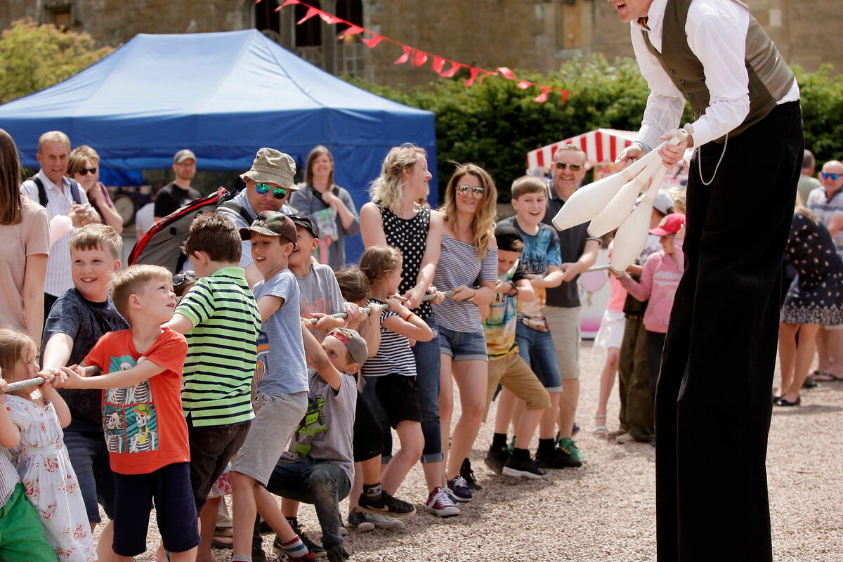 Juggler on stilts performing for a crowd at Eastnor Vintage