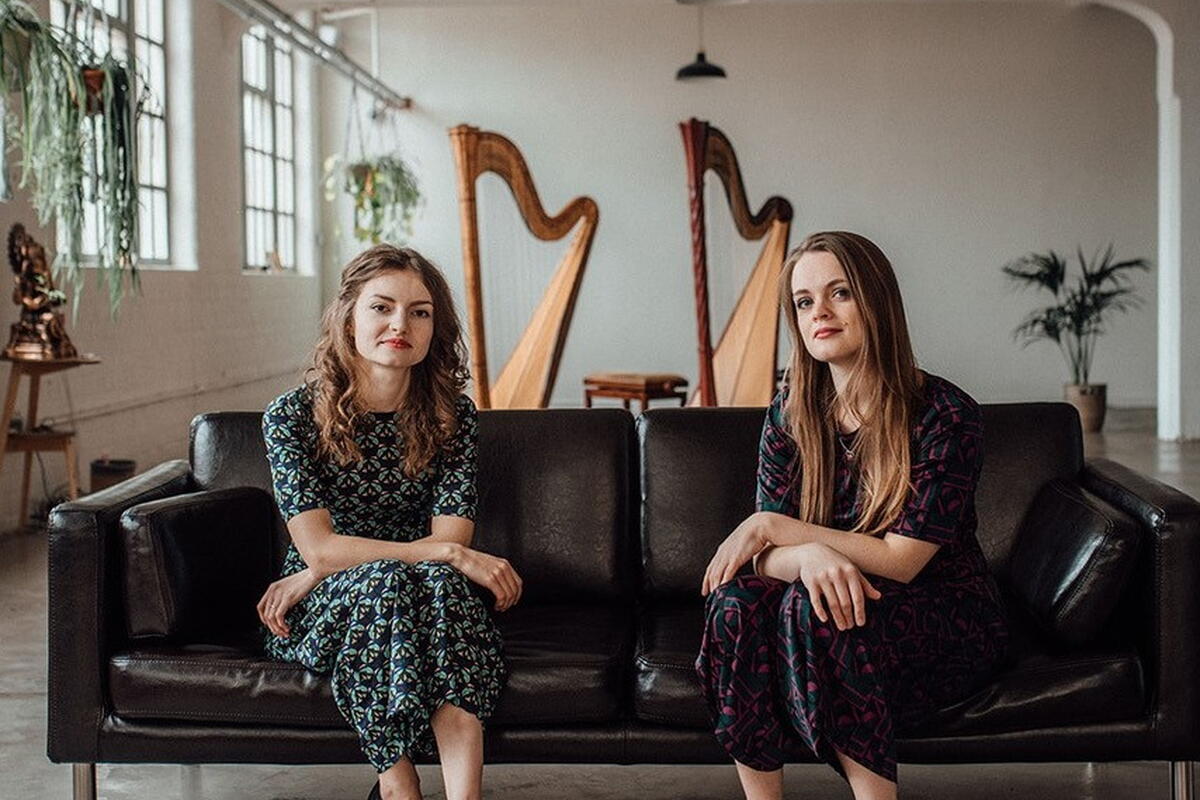 2 ladies sitting on couch with harps in the background