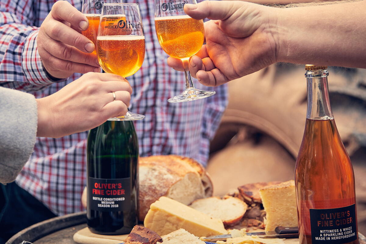 glasses of cider being raised over table with cheese and crackers