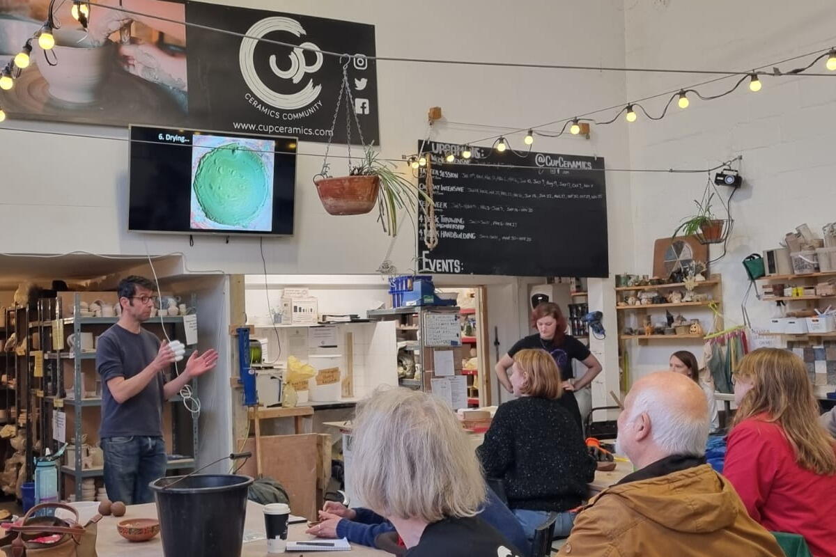 Person giving a talk to a room full of people at pottery workshop