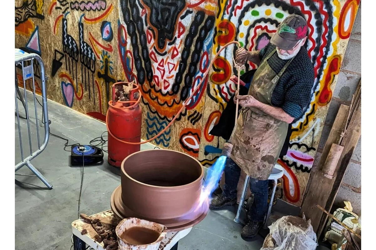 Man with blowtorch and large red clay pot on potter's wheel