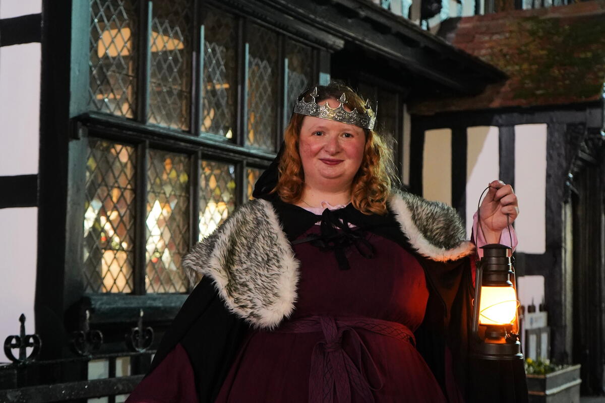 Person dresses in costume and crown holding a lantern