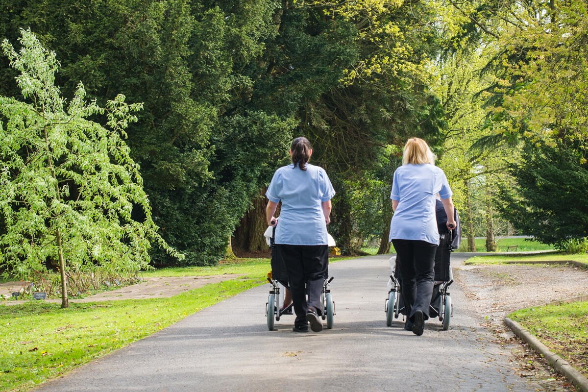 people in wheelchairs with support staff walking down a wide path
