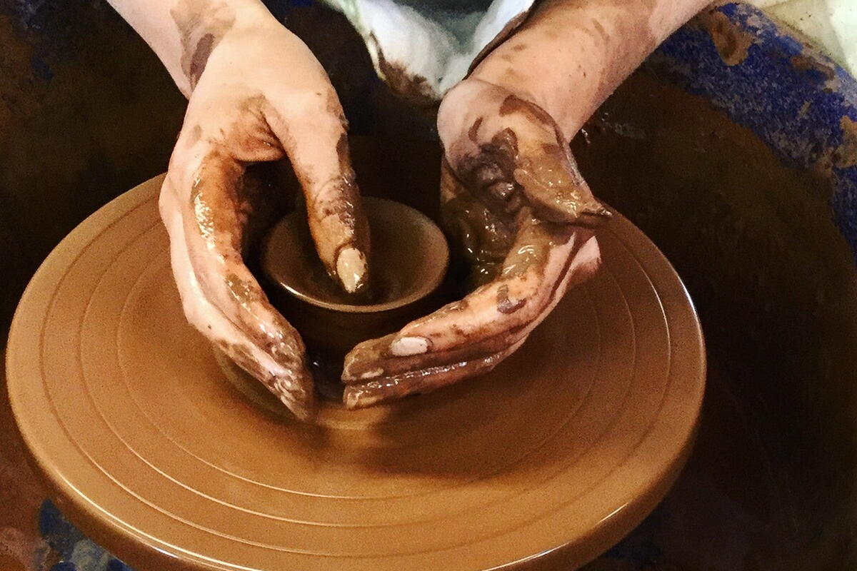 hands on a clay pot on a potter's wheel