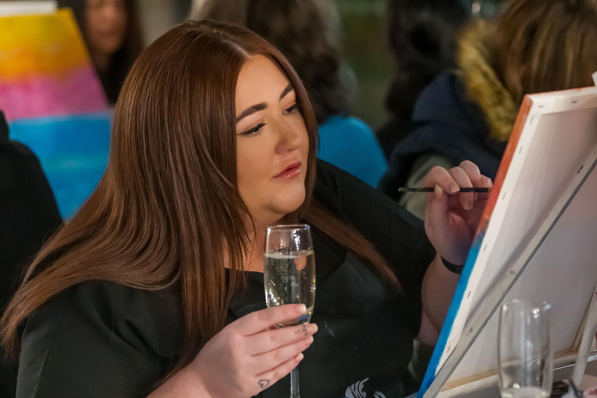 Person holding glass of bubble sat in front of a canvas painting