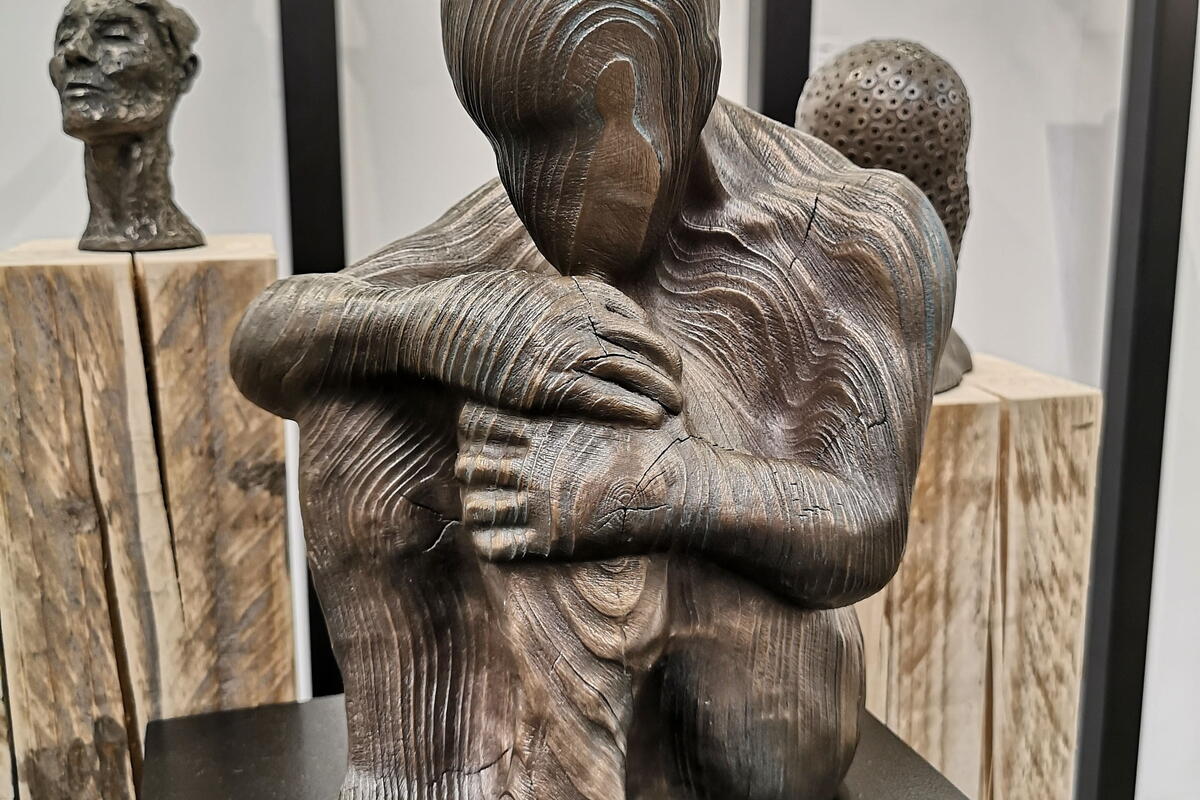 wooden carved sculpture of a person sitting holding their knees to their chest