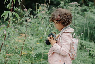 girl taking a photograph in a green flower meadow