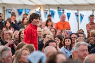 A person giving a presentation in a marquee full with a seated audience 