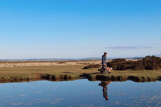 Young woman walking dog reflected in pond on high up landscape