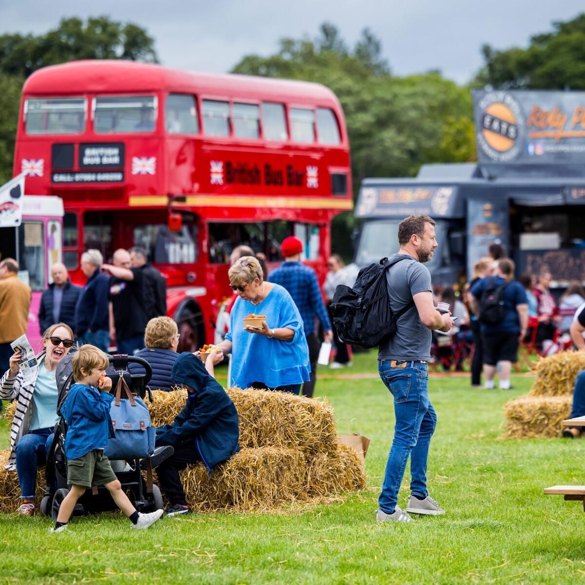 people sitting on hay bales at festival with red London bus