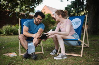 A male and female sitting on Ledbury Poetry branded deckchairs and reading a book together