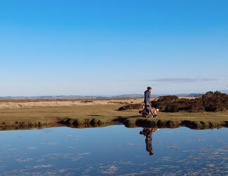 Young woman walking dog reflected in pond on high up landscape