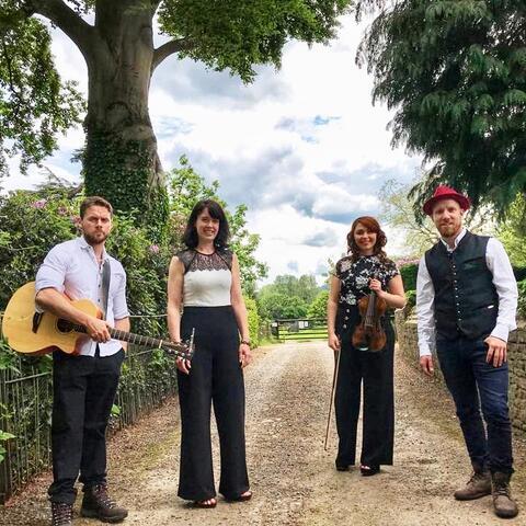 The four members of The Kilpecks standing on a country lane with their musical instruments