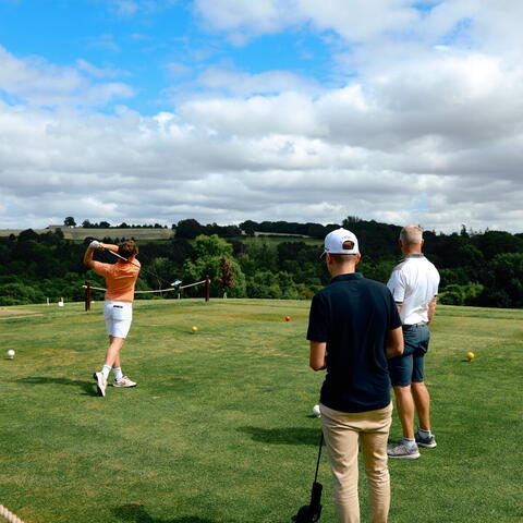 three people standing on golf course overlooking hilly countryside