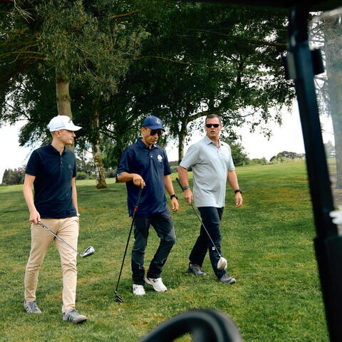 three people walking across golf course carrying golf clubs