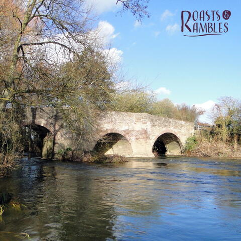 ancient bridge with river flowing through, trees to one side and bright blue skies