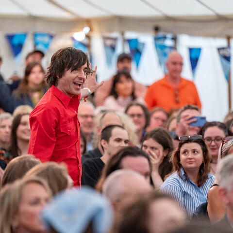 A person giving a presentation in a marquee full with a seated audience 