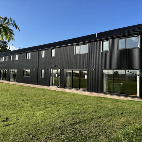 black barn conversion against blue sky with green grass below