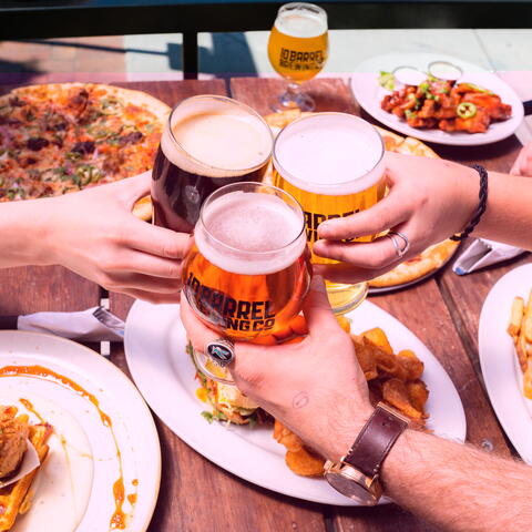 3 people cheersing beers with plates of chips and burgers on the table