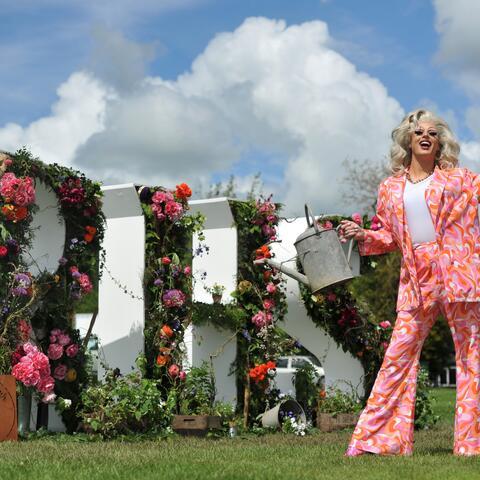 Person dressed in pink suit in front of RHS letters made of flowers