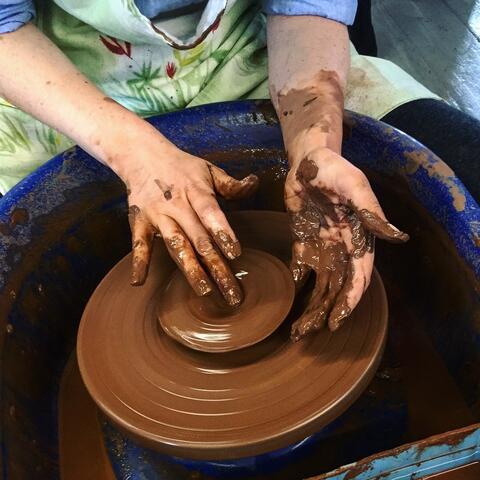 Person shaping red clay pot on a potters wheel