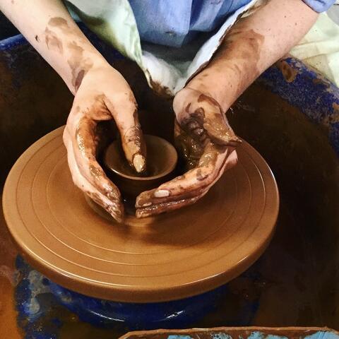 close up of hands working red clay pot on potter's wheel
