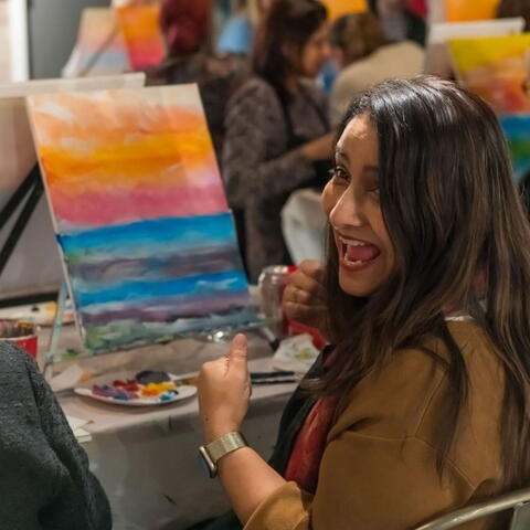 woman with dark hair taking part in a painting workshop with a canvas on an easel in front of her