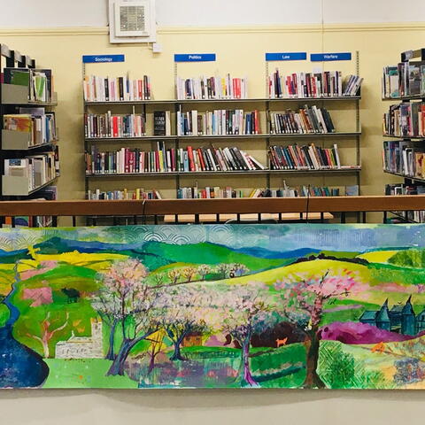books on shelves above a mural on a wall