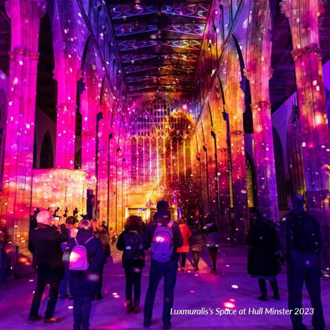 solar system images projected onto the walls and ceiling inside a cathedral with pinks, blues, purple and yellow hues