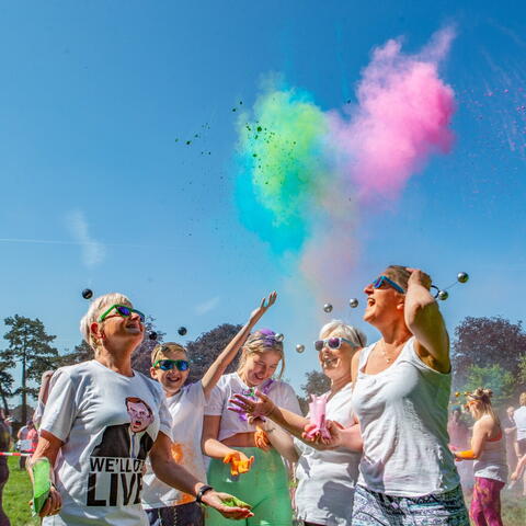 Festival goers throwing coloured powder in the air on a sunny day