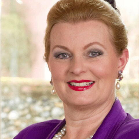 Person with blond hair, red lipstick wearing a purple blazer