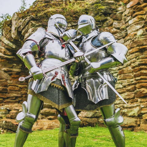 Two knights in full armour clashing swords in castle grounds