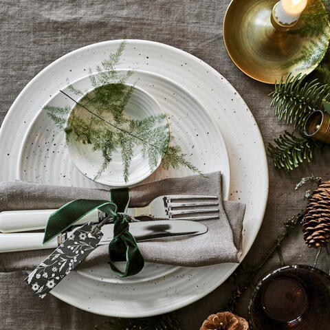 Christmas table setting with white crockery, a rolled white linen napkin and green foliage