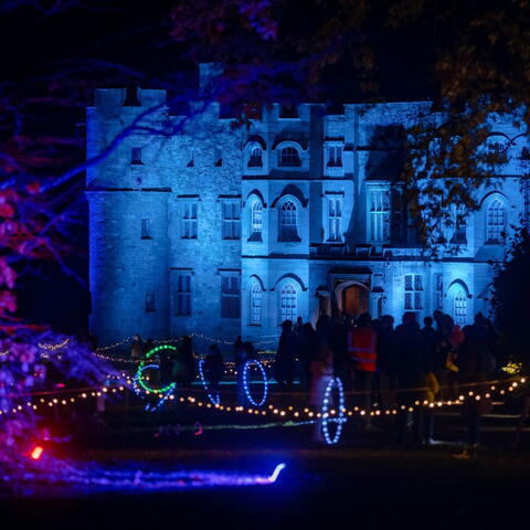 Croft castle illuminated with blue light projections on castle walls and coloured lights in trees