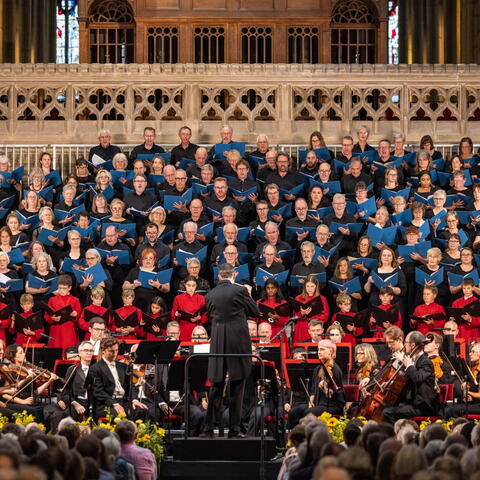 Large choir in black and red robes holding blue songbooks